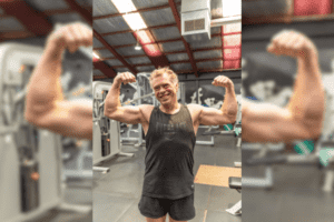Brendan, a 57-year-old member of Genesis Ballarat, flexes his muscles while smiling in the gym.