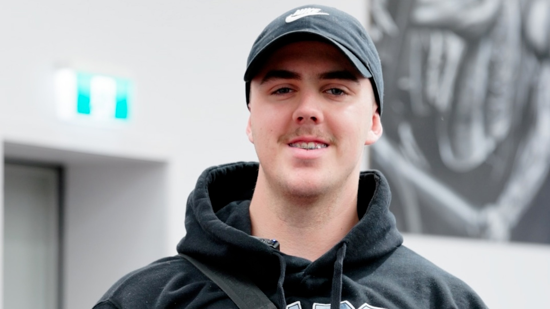A young man named Baily is smiling in front of a blurred background. He is wearing a black hoodie and a cap. The image features the text: "GOOD COMMUNITY, GOOD CULTURE & THEY GIVE OPPORTUNITIES - BAILY," emphasising his positive experience at Genesis Ballarat and the supportive environment he appreciates.
