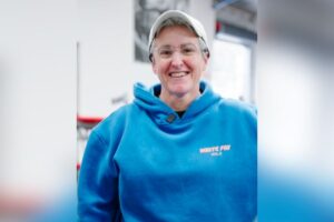 Sally, a happy and long-time member of Genesis Ballarat, smiling warmly, radiating a sense of joy and belonging in the supportive gym community, with fitness equipment visible in the background.
