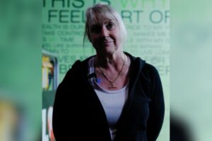 Nicole, a long-time member of Genesis Ballarat, standing in the gym, wearing a black hoodie and white tank top, sharing her inspiring fitness journey and experiences with rehabilitation through tailored workouts.