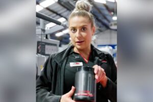 Pricilla from Nutrition Warehouse holding a supplement container inside Genesis Ballarat gym, offering free samples and expert nutrition advice to members as part of their collaboration.